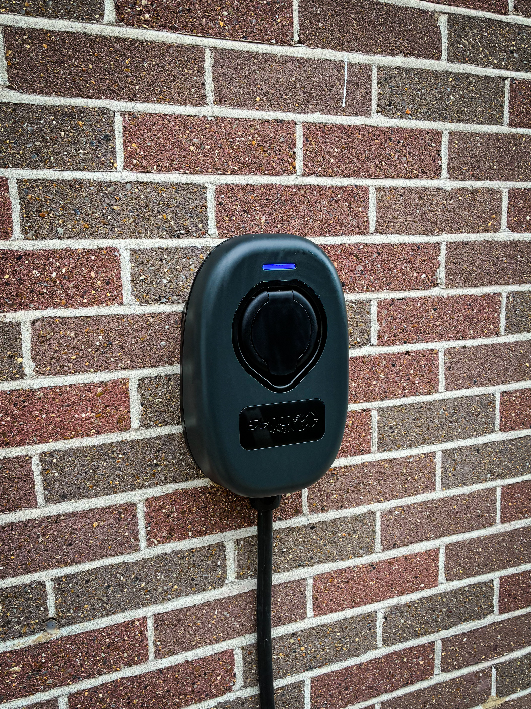 Installed home EV charge point with the status light glowing on a brick wall
